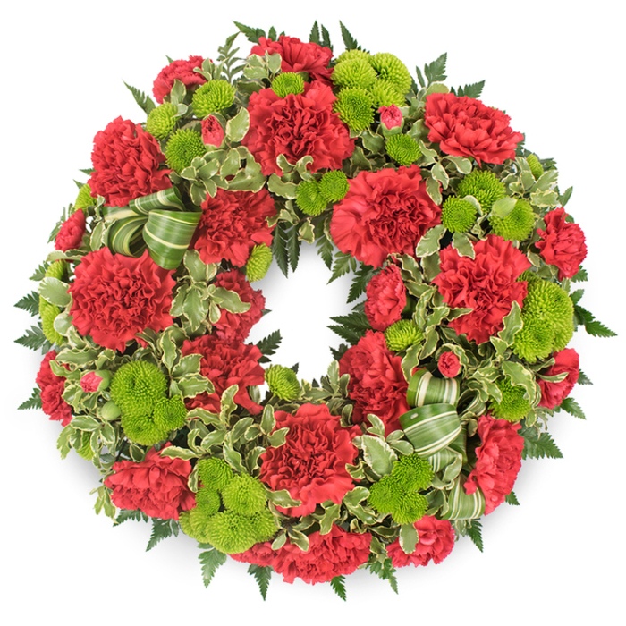 In this image, a large, circular funeral wreath is presented against a stark white backdrop, allowing its rich red and green palette to stand out vividly, like a focal point in a serene Harold Park chapel. The wreath itself is densely packed, so full that no underlying structure is visible, creating a sense of abundance and devoted craftsmanship. At the heart of the design are numerous deep red carnations, each blossom composed of rumpled, layered petals that fold and ripple inwards, giving the flowers a soft, almost plush texture. Some carnations are fully open, spreading wide across the surface, while others are more compact, suggesting newer blooms just beginning to unfurl. Woven throughout these crimson flowers are bright lime green button chrysanthemums, or pompon mums, forming perfectly round, textured discs. Their vivid chartreuse tone adds a refreshing brightness and a contemporary twist to the otherwise classic red-and-green scheme, as if bringing a breath of fresh air from the nearby Harold Park open spaces. Encircling and cradling the flowers is a base of mixed foliage: deep green fern fronds arch outward, creating a feathery outer halo, while variegated pittosporum leaves, with creamy edges and darker centers, introduce a delicate patterned effect that softens the wreath's silhouette. Tucked into the lower portion is a tasteful decorative accent-a wide ribbon or leaf-like material striped in light and darker green-shaped into graceful loops that sit comfortably among the greenery. The even, diffused lighting and the faint shadow cast below the wreath make it appear slightly lifted from the background, lending depth and quiet dignity. Overall, the arrangement conveys solemn respect, loving remembrance, and a gentle sense of peace, ideal for funerals, wakes, or graveside tributes for families across Harold Park.